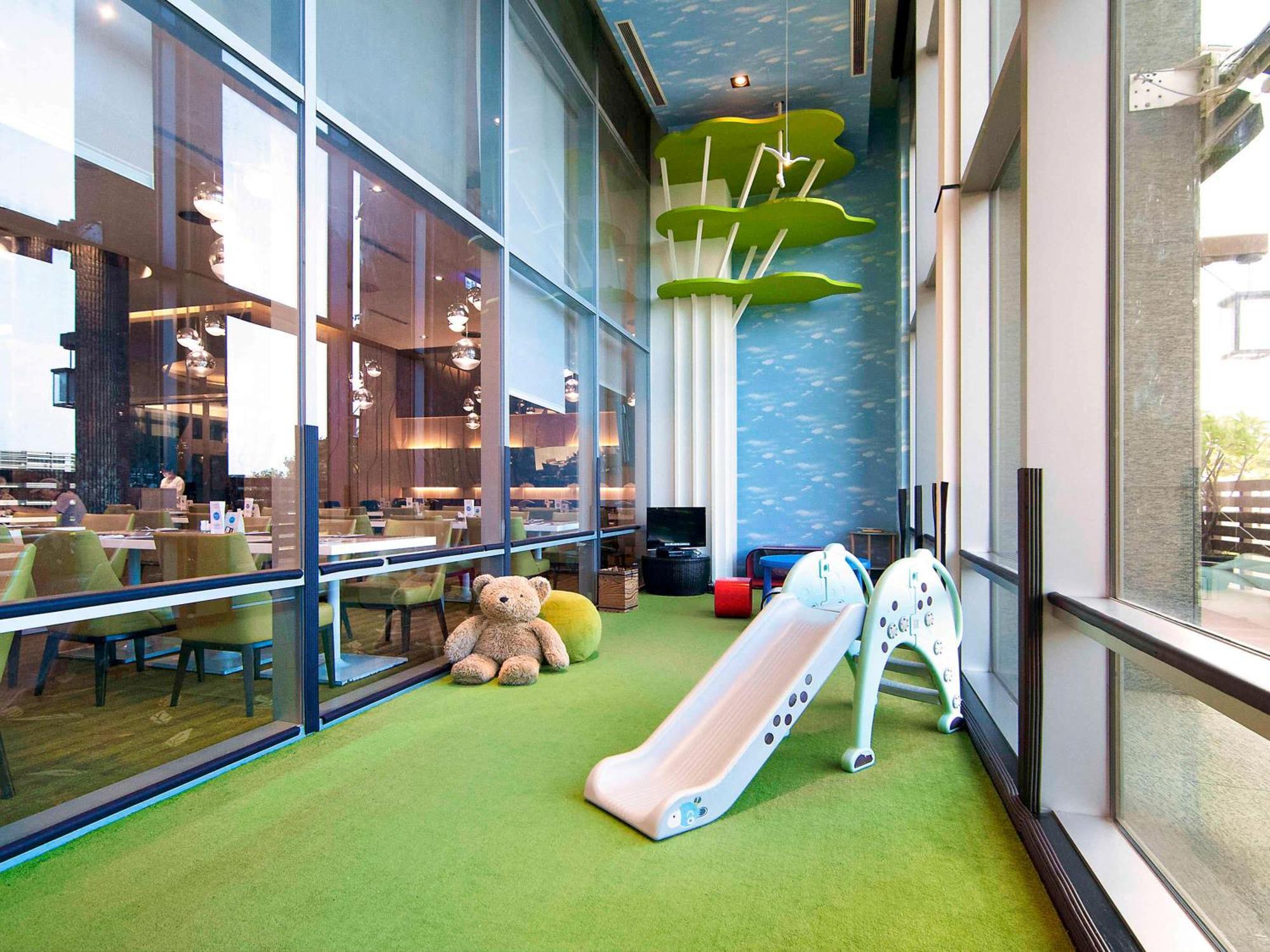 Hyatt Regency Taoyuan International Airport Hotel Exterior photo The photo depicts a children's play area that features a small slide, which is designed to look like a giraffe. The flooring is covered in green turf, providing a soft and safe surface for children to play on. In the background, there are large windo