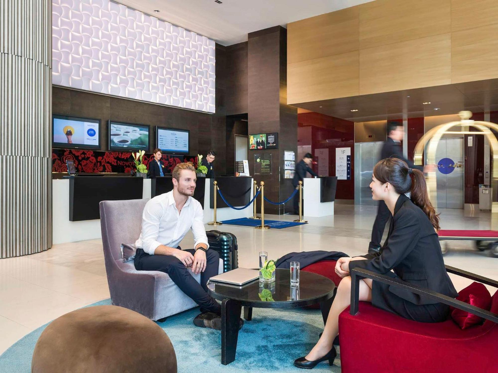 Hyatt Regency Taoyuan International Airport Hotel Exterior photo The photo shows a modern hotel lobby. In the foreground, a man dressed in a casual white shirt is sitting in a comfortable chair, engaging in conversation with a woman wearing a professional black outfit. They are seated at a small round table, which