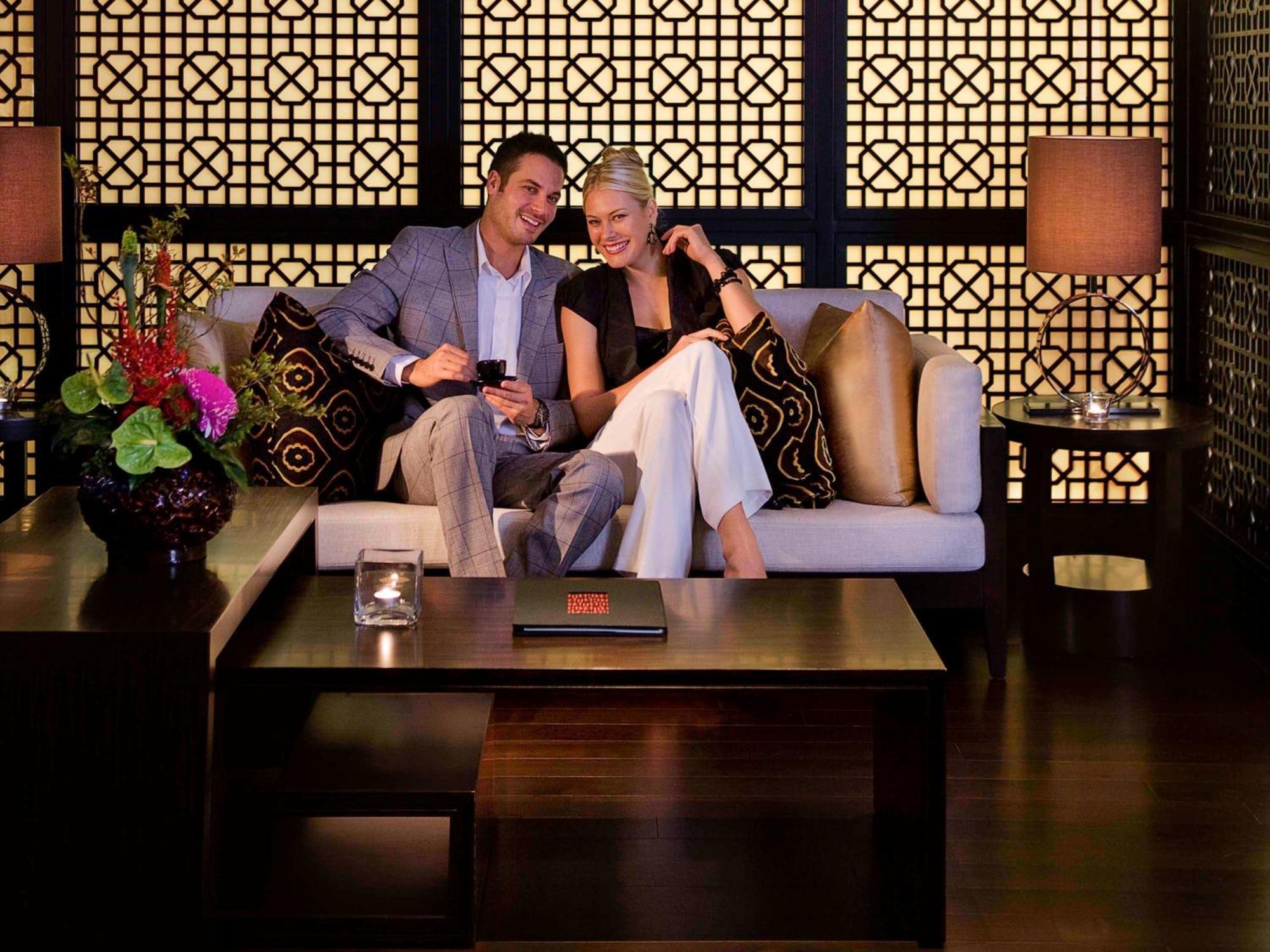 Hyatt Regency Taoyuan International Airport Hotel Exterior photo The photo depicts a stylish interior setting with a couple sitting on a modern sofa. The man is dressed in a light gray suit, while the woman is wearing a black and white outfit. They appear to be enjoying each other's company, possibly sharing a dri