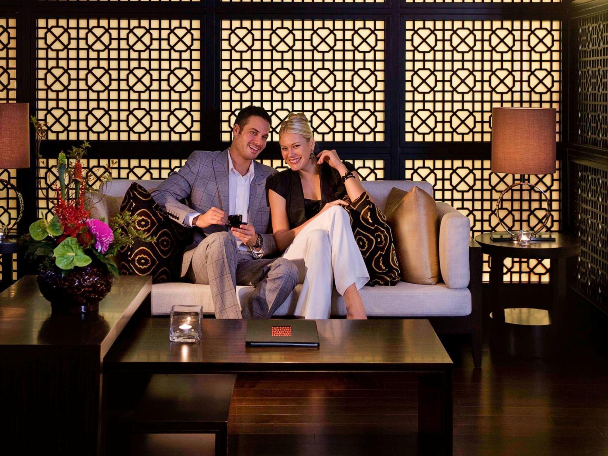 Hyatt Regency Taoyuan International Airport Hotel Exterior photo The photo depicts a couple sitting together on a stylish sofa in a cozy, well-lit setting. They appear to be enjoying each other's company, smiling, and looking at something on a smartphone. The background features an intricate lattice design, castin